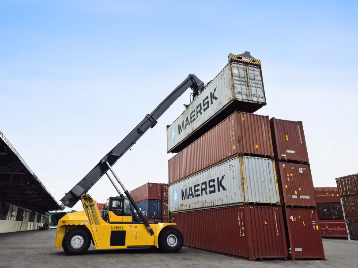 "Reach stacker in action lifting and stacking shipping containers at a busy port terminal, showcasing its powerful telescopic boom and maneuverability."